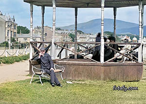 Victorian image that has been restored, colourised amd HD enhanced of an elderly gentleman sitting near the bandstand enjoying Warrenpoint seafront